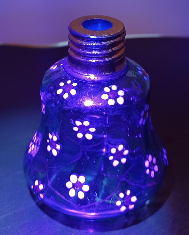 May include: A blue glass bottle with a floral pattern. The bottle has a flared base and a threaded neck. White flowers are painted on the surface, and the bottle has a gold-coloured rim.