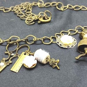 May include: A gold chain necklace with various charms, including a thimble, scissors, a spool of thread, a dress form, and a small bottle. The charms are all in a vintage style.