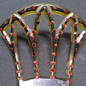 May include: A vintage hair comb with a yellow plastic base and black accents. The comb is decorated with red rhinestones.
