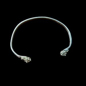 May include: A silver-toned open cuff bracelet featuring a smooth, curved band that terminates at both ends in detailed, textured clusters resembling small, rounded berries or floral buds, creating a distinct contrast in surface finish.