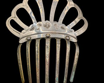 May include: A silver-toned metal hair comb with a crown-like design. The comb features a fan-shaped top with floral and dot details, and vertical tines. The metal has a slightly aged appearance.