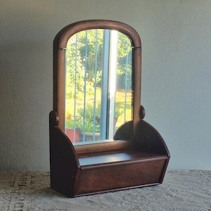 May include: A dark brown wooden vanity mirror featuring an arched top frame and a rectangular base with a flat shelf. The mirror is mounted on two side supports, allowing for a vertical orientation. The wood has a smooth, polished finish.