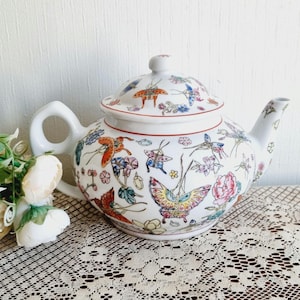 May include: White porcelain teapot with a floral and butterfly design. The teapot has a lid and a spout. The design features colourful butterflies and flowers on a white background.