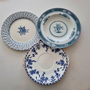 May include: Three ceramic plates with blue and white patterns. One plate features a central rose, another a central floral vase with a geometric border, and the third a floral vine design with gold-toned handles on opposite sides of the rim.