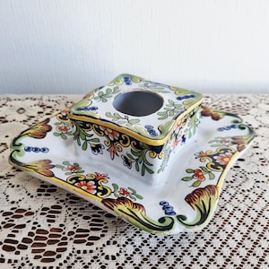 May include: A white ceramic tissue box holder with a square top and a matching rectangular base. The holder and base are decorated with colorful floral and leaf patterns in red, yellow, green, and blue. The edges are trimmed with yellow and blue.