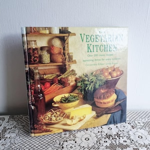 May include: A cookbook titled "The Vegetarian Kitchen" with a cover featuring a still life of vegetables and prepared dishes. The cover includes text and images of ingredients like onions, cheese, and bread, with over 200 recipes.
