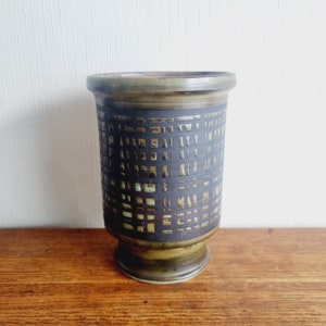 Può includere: Un vaso in ceramica verde con un motivo geometrico nero. Il vaso ha una base larga e un'apertura stretta.