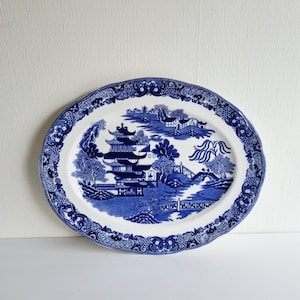 May include: Oval blue and white ceramic platter with a Willow pattern design. The platter features a central scene of a pagoda, bridge, and trees, surrounded by a decorative border. The platter is approximately 14 inches long.