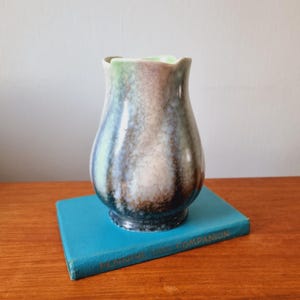 Peut inclure: Un vase en céramique de forme bulbeuse avec un glaçage marbré dans des tons de vert, bleu et marron. Le vase a un bord légèrement évasé et une base arrondie.