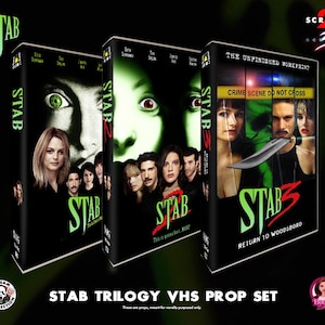 May include: A set of three VHS tapes from the "STAB" trilogy, with the titles "STAB", "STAB 2", and "STAB 3". The tapes feature images of actors and the text "STAB" in a green, stylized font. The set is labeled "STAB TRILOGY VHS PROP SET".