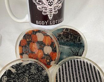 May include: Set of four round coasters with different Halloween-themed designs. The coasters are made of clear resin with glitter embedded in the resin. The designs include pumpkins, a spooky house, a striped pattern, and a black and white floral pattern with ghosts.