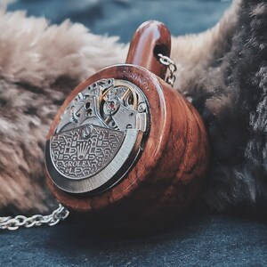 May include: A wooden pendant with a silver watch face and gears visible. The pendant is attached to a silver chain.