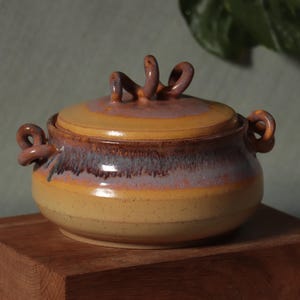 May include: A set of three ceramic mugs with a speckled, matte finish in cream, light brown, and dark brown. Each mug has a simple, minimalist design and a rounded handle.