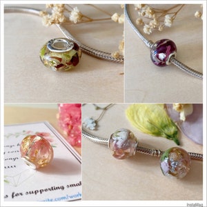 May include: A collection of clear resin beads with dried flowers and metallic accents. The beads are round with a silver-colored core and are strung on a silver chain. The beads contain various colors of dried flowers.