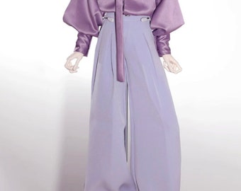 May include: A doll wearing a purple satin blouse with a long tie and matching purple wide-leg pants. The doll has short, silver hair and is wearing white sneakers.