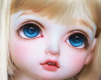 May include: A close-up of a porcelain doll with long, straight blonde hair and blue eyes. The doll has a delicate facial features and is wearing a white dress.