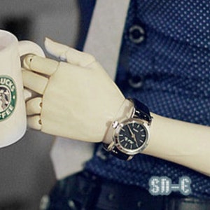 May include: A person wearing a blue patterned button-down shirt with a white tie and a black leather belt. They are holding a white coffee mug with the Starbucks logo and a silver watch on their wrist.