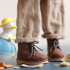 Op de afbeelding: Een bruine corduroy jas voor poppen met houten knopen en een bruine corduroy broek voor poppen met bruine leren laarzen.
