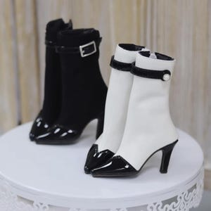 Könnte beinhalten: Ein Paar schwarze und weiße Stiefeletten mit Absatz, spitzer Zehenpartie und Schnallen-Detail. Die Stiefeletten haben eine schwarze Lackleder-Zehenpartie und einen schwarzen Lackleder-Absatz.