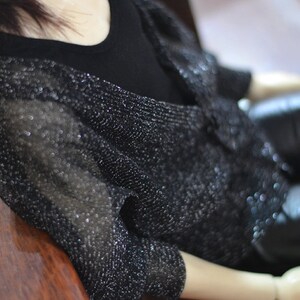 May include: A black sparkly cardigan with a long sleeve and a black top underneath.
