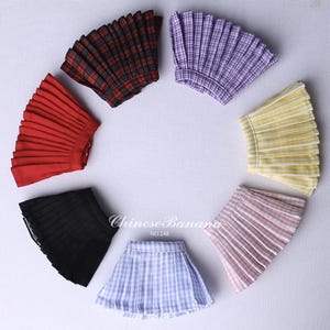 Op de afbeelding: Een verzameling van acht miniatuur geplooide rokken in verschillende kleuren en patronen, waaronder rood, zwart, ruitjes en pastelstrepen. De rokken zijn in een cirkelvormig patroon gerangschikt, waarbij hun verschillende ontwerpen worden getoond.
