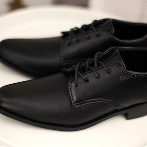 May include: A pair of black leather lace-up shoes with a pointed toe. The shoes are on a white surface.