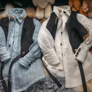 May include: Two miniature shirts with black waistcoats and gold buttons. One shirt is light blue and the other is white. Both shirts have long sleeves and are made of a soft, textured fabric.