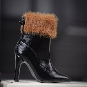 Könnte beinhalten: Ein schwarzer High-Heel-Stiefel mit spitzer Zehenpartie und einem flauschigen braunen Pelzbesatz am oberen Rand. Der Stiefel hat ein glänzendes Finish und einen schlanken Absatz.
