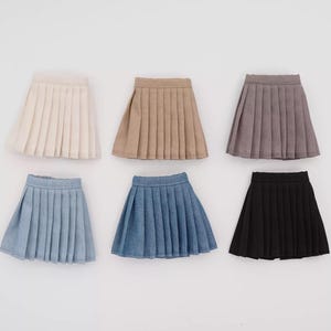 May include: Six pleated mini skirts in various colors: cream, tan, mauve, light blue denim, dark blue denim, and black. The skirts are arranged in two rows of three, showcasing their different hues and textures.