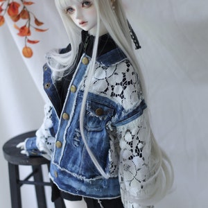 May include: A white doll with long, straight, white hair wearing a blue denim jacket with white lace sleeves and a black skirt.