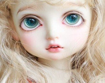May include: A close-up of a porcelain doll with blonde hair and blue eyes. The doll is wearing a pink and white dress.
