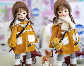 May include: Two dolls wearing yellow coats with brown hats and white accents. The dolls are holding stuffed animals and are standing next to a red toy wagon.