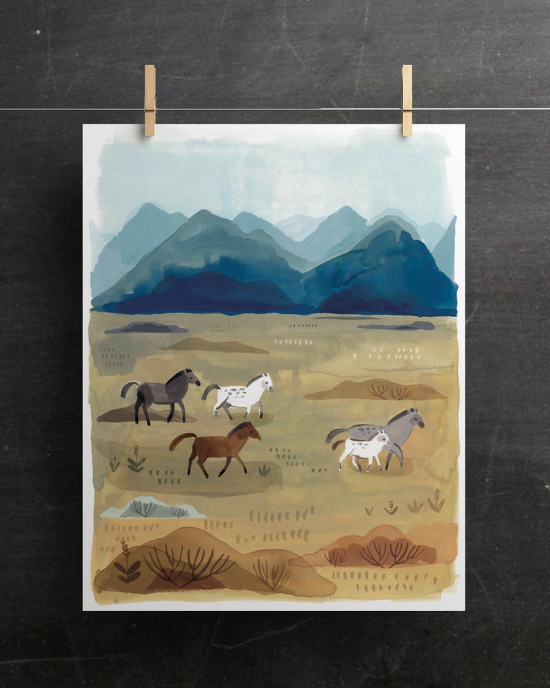 Puede incluir: Impresi&oacute;n en acuarela de un paisaje con una manada de caballos en un campo, con un tel&oacute;n de fondo de monta&ntilde;as azules. Los caballos son de varios colores, incluyendo marr&oacute;n, gris y blanco. La impresi&oacute;n est&aacute; sujeta con pinzas de madera.