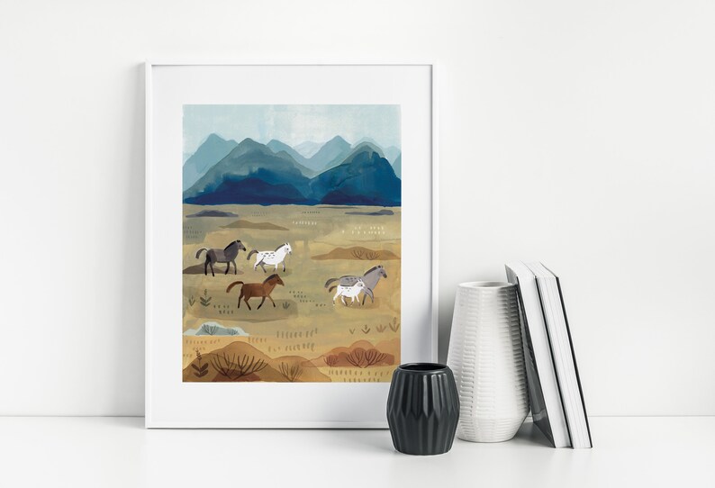 Puede incluir: Una impresi&oacute;n art&iacute;stica enmarcada que presenta un paisaje con caballos corriendo. La obra de arte representa una manada de caballos en tonos marrones, grises y blancos, sobre un fondo de monta&ntilde;as azules y un campo beige. La impresi&oacute;n est&aacute; en un marco blanco.