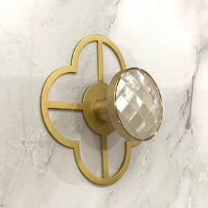 May include: Two gold-toned decorative hooks with a quatrefoil design. Each hook features a round, clear, faceted crystal knob.