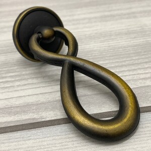 Könnte beinhalten: Ein schwarzer und goldener Kabinettgriff in Form einer Unendlichkeitsschleife mit runder Basis.