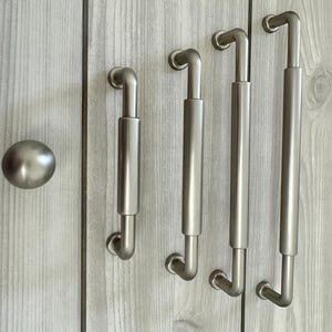 May include: A set of brushed nickel cabinet hardware including one round knob and four varying lengths of cylindrical bar pulls. Each pull features a central thicker barrel section with slender mounting posts at both ends, mounted vertically.
