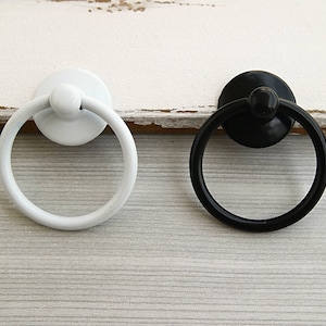 May include: Two door pulls, one black and one white, with a round knob on the top. The pulls are made of metal and have a simple design.