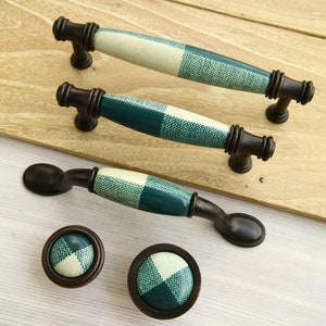 Può includere: Set di quattro pomelli e maniglie per armadi in ceramica a scacchi verdi e bianchi con finitura bronzo. I pomelli e le maniglie hanno un motivo quadrato.