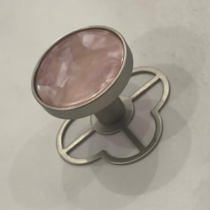 Può includere: Un pomello decorativo per mobili con un centro rosa a forma ovale e una base in metallo color argento. La base ha un design a forma di trifoglio. Il pomello è progettato per l'uso su cassetti o armadi.