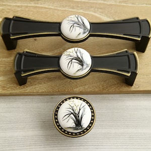 May include: Three black and gold cabinet knobs with white ceramic inserts featuring a floral design. The knobs are in various sizes.
