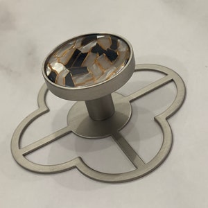May include: A silver metal hook with a decorative, round, black and white patterned knob. The hook is attached to a four-leaf clover shaped base.