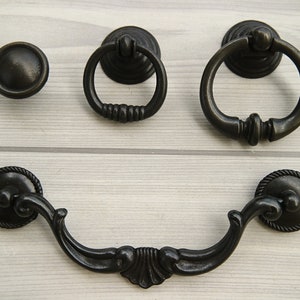 May include: Four black metal cabinet knobs and pulls. One is a round knob, one is a ring pull, and two are ornate pulls with a curved handle.