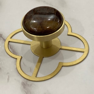 May include: Gold cabinet knob with a brown stone top and a four-leaf clover shaped base.
