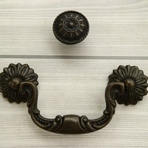 Könnte beinhalten: Antiker Bronze-Schrankgriff mit verzierten floralen Details. Der Griff hat einen dekorativen, gebogenen Griff und zwei passende Rosetten.