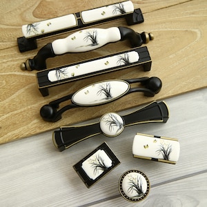 Puede incluir: Surtido de pomos y tiradores de armario negros y dorados con inserciones de cerámica blanca con un diseño floral con mariposas.