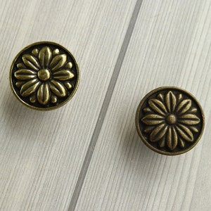 Puede incluir: Dos pomos de armario de color dorado antiguo con un diseño floral.