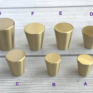 May include: Seven gold-toned metal cabinet knobs in various sizes. The knobs are cone-shaped with a smooth, brushed finish.