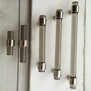 May include: Four different sizes of clear glass cabinet pulls with a silver finish. The pulls are all cylindrical in shape and have a smooth, polished surface.