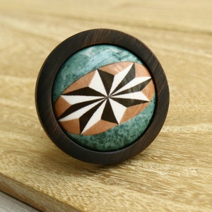 Puede incluir: Un pomo redondo de madera con un diseño geométrico en blanco y negro sobre un fondo turquesa. El pomo tiene un marco de madera marrón oscuro.